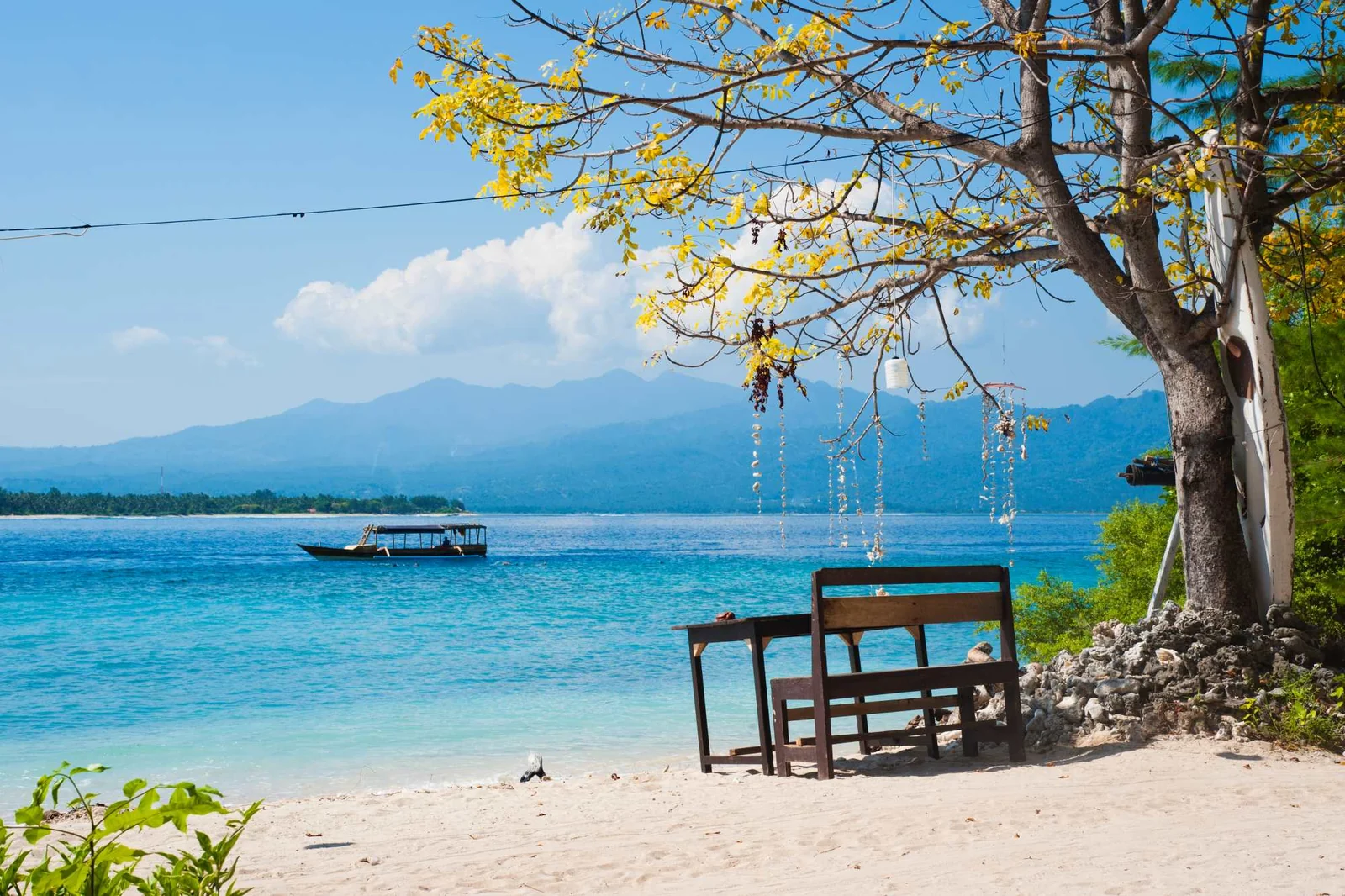 A quiet beach on Gili Air: white sand, a wooden bench under a tree and a boat on turquoise water